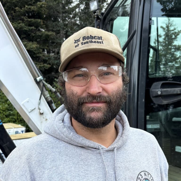 Man wearing a cap and safety glasses standing next to an excavator