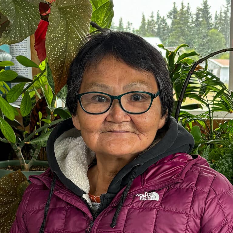 Woman with glasses and a purple North Face Coat in front of plants inside
