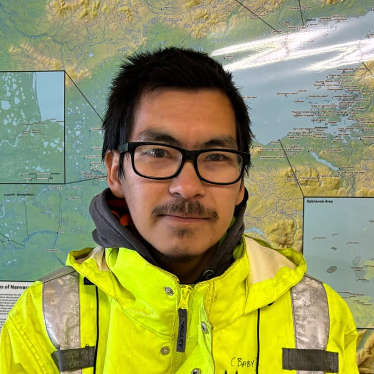Man with glasses and neon yellow coat in front of a map of Alaska