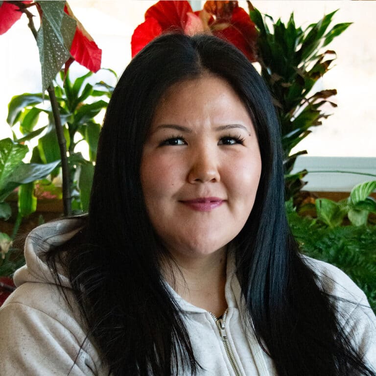 Woman with black hair standing in front of plants smiling